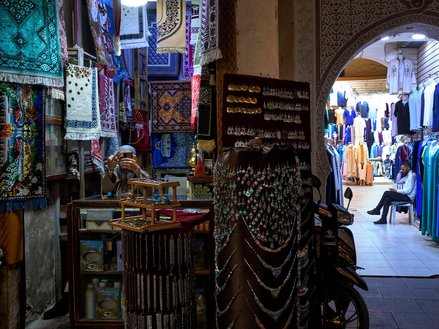 Colorful Moroccan bazaar with textiles, jewelry, and traditional clothing displayed in a vibrant market stall.