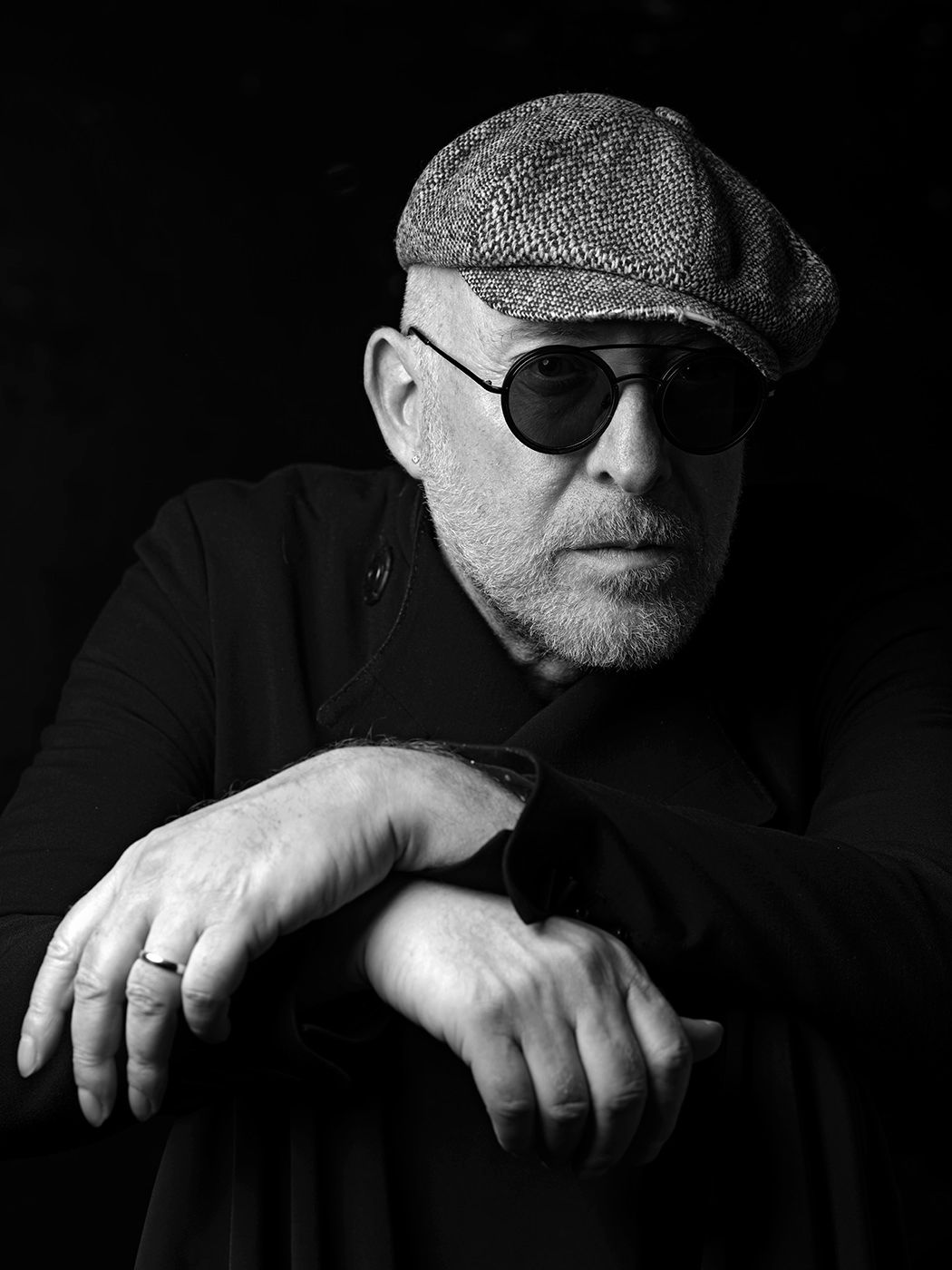 Black and white portrait of an older man wearing a flat cap and round sunglasses, arms crossed. Mario Biondi