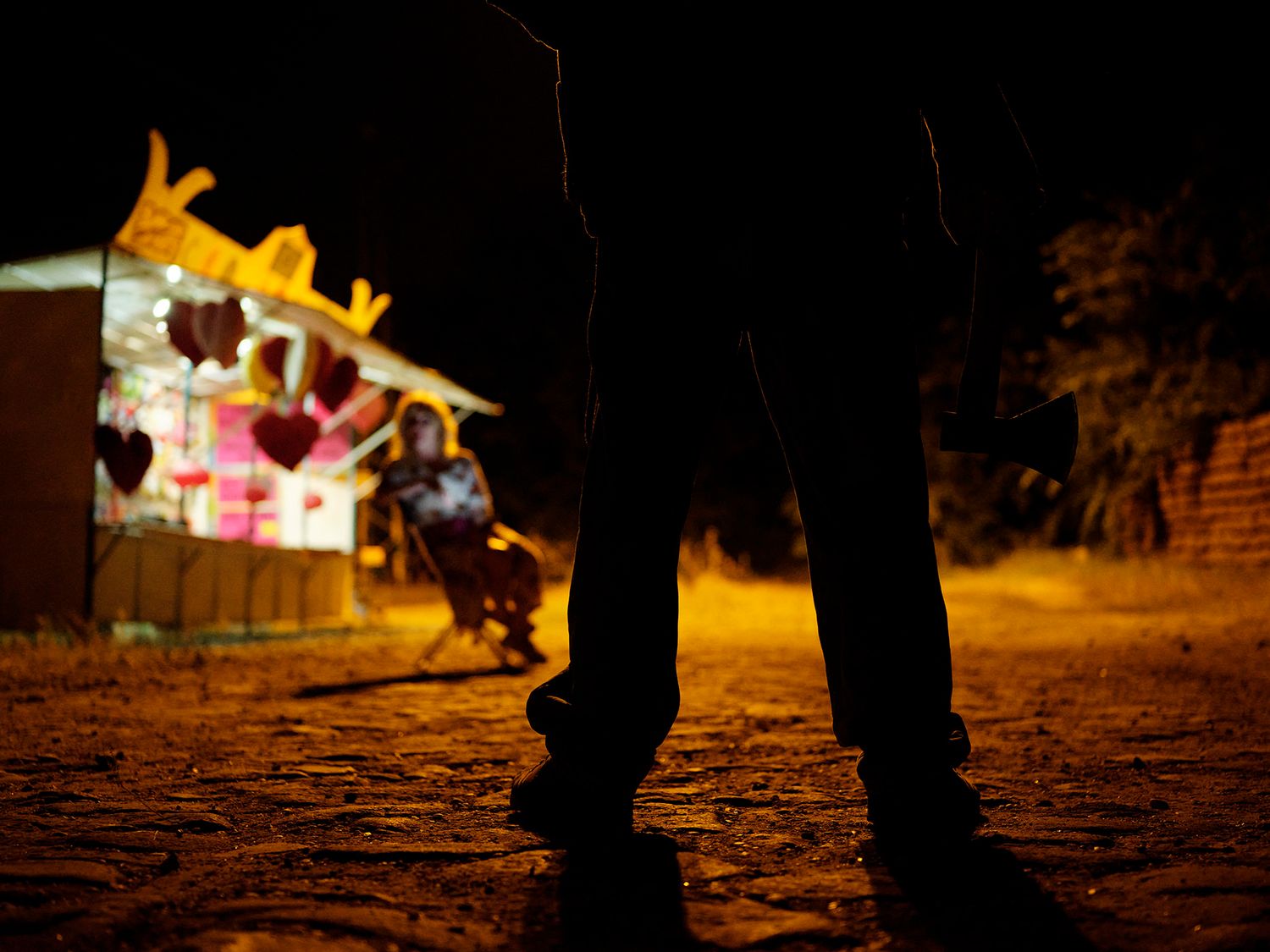 Silhouette of a person standing before a colorful illuminated heart-decorated building at night.