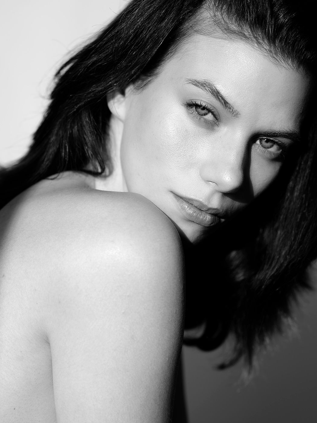 Black and white portrait of a young woman with dark hair looking over her shoulder with a soft, confident expression.