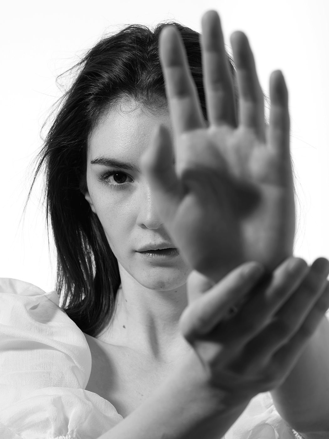 Black and white portrait of a young woman holding her hand up toward the camera in a stop gesture.