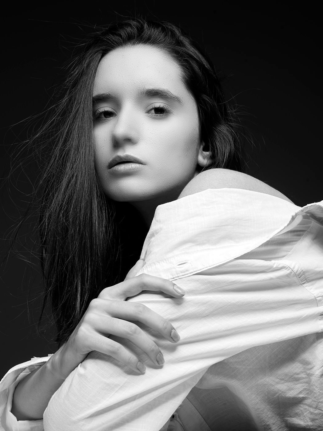 Black and white portrait of a young woman with dark hair wearing a white oversized shirt, studio photography.