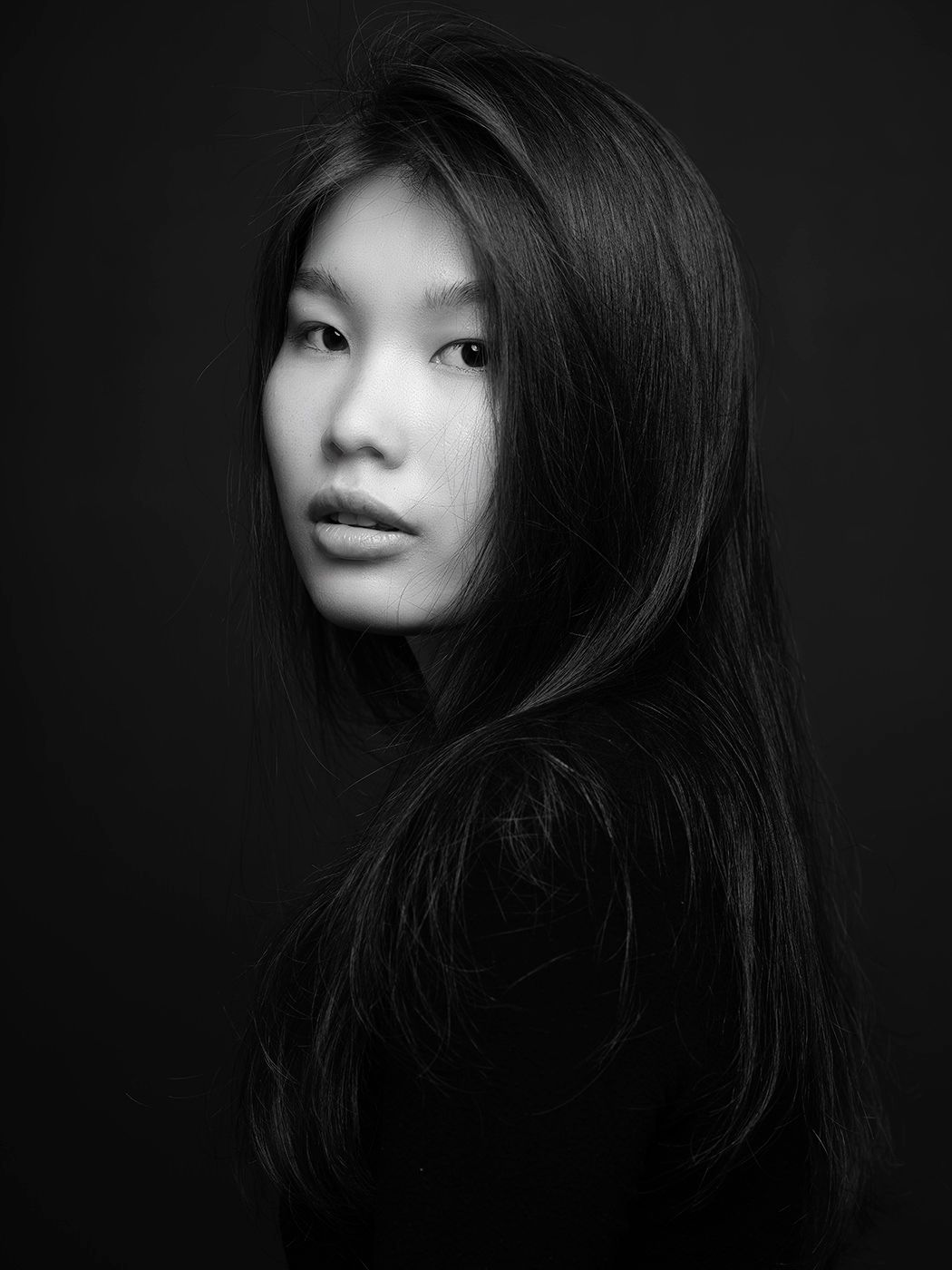 Black and white portrait of a young Asian woman with long dark hair against a dark background.