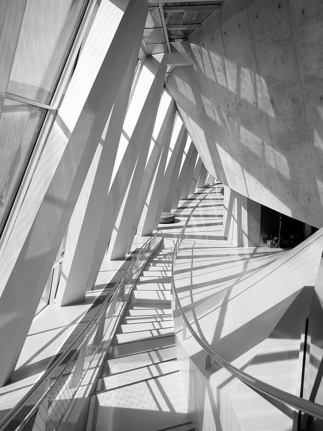 Black and white interior architectural photo showing dramatic diagonal lines, shadows, and geometric shapes in a modern building.
