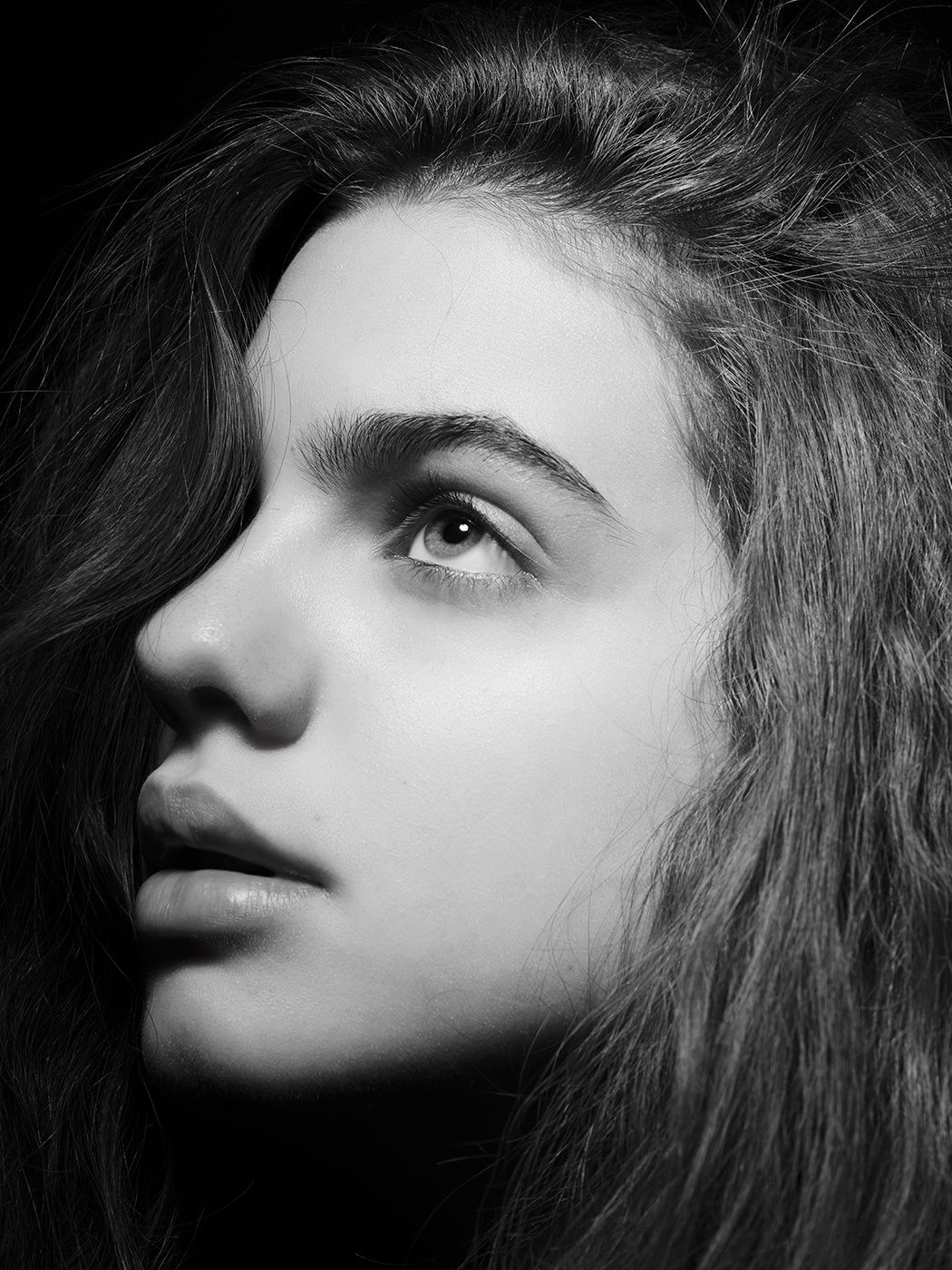 Black and white portrait of a young woman with long hair, gazing upward with a contemplative expression.