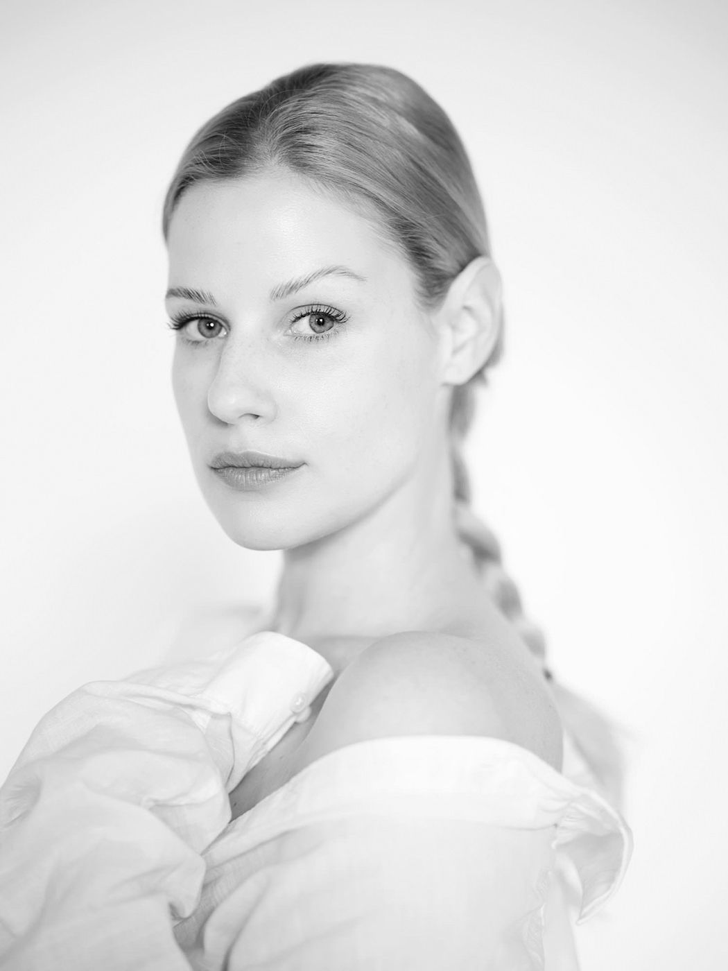Black and white portrait of a young woman with a braided ponytail wearing an off-shoulder white top.