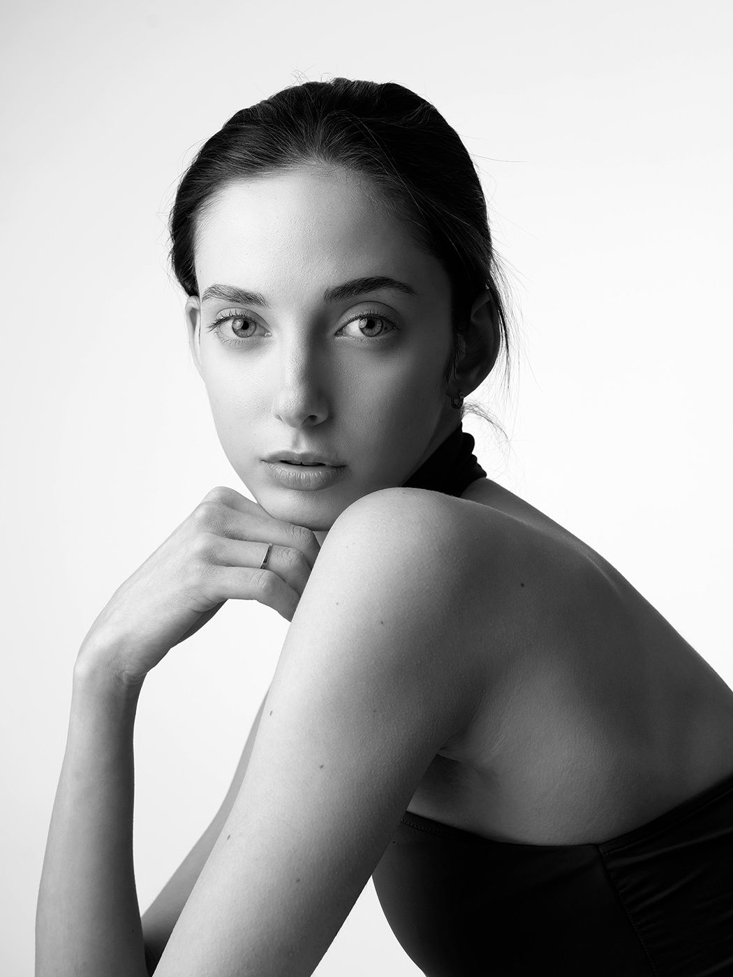 Black and white portrait of a young woman with dark hair, bare shoulders, resting chin on hand.