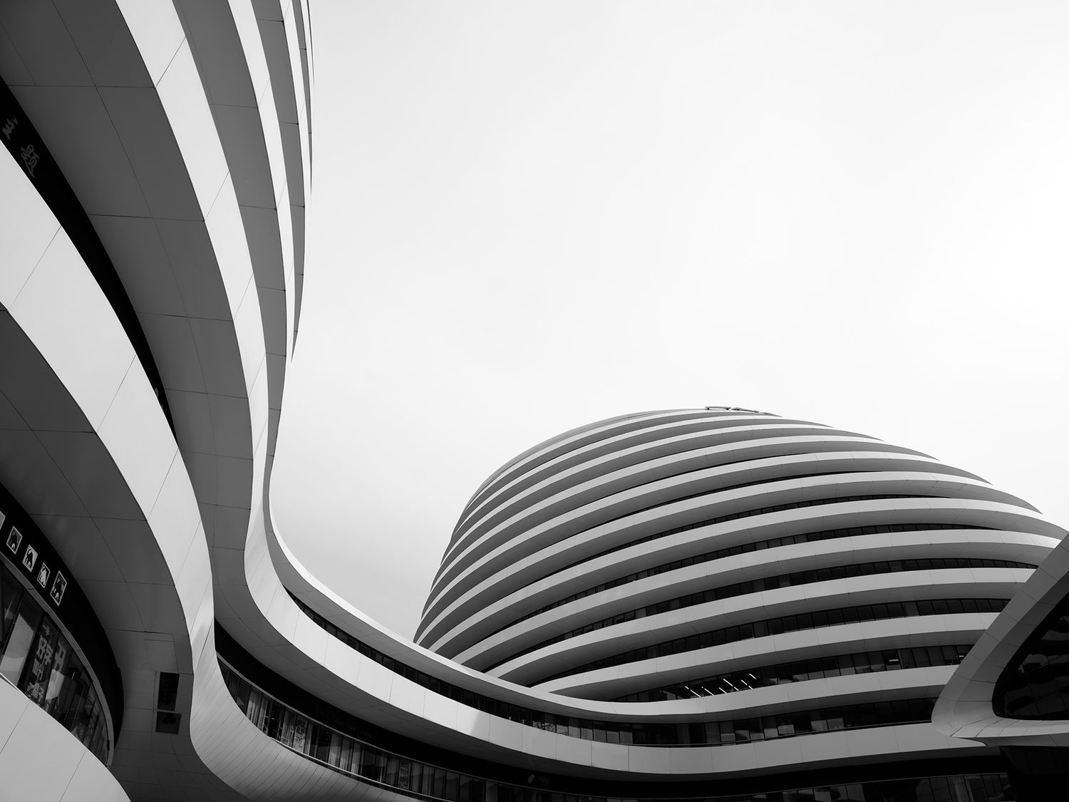Black and white low-angle shot of a modern curved skyscraper with sweeping architectural lines against a gray sky.