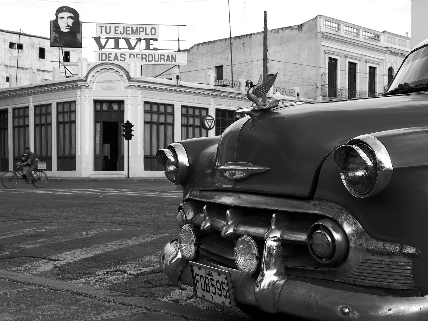 Vintage American car parked on a Cuban street with a Che Guevara mural in black and white photography.