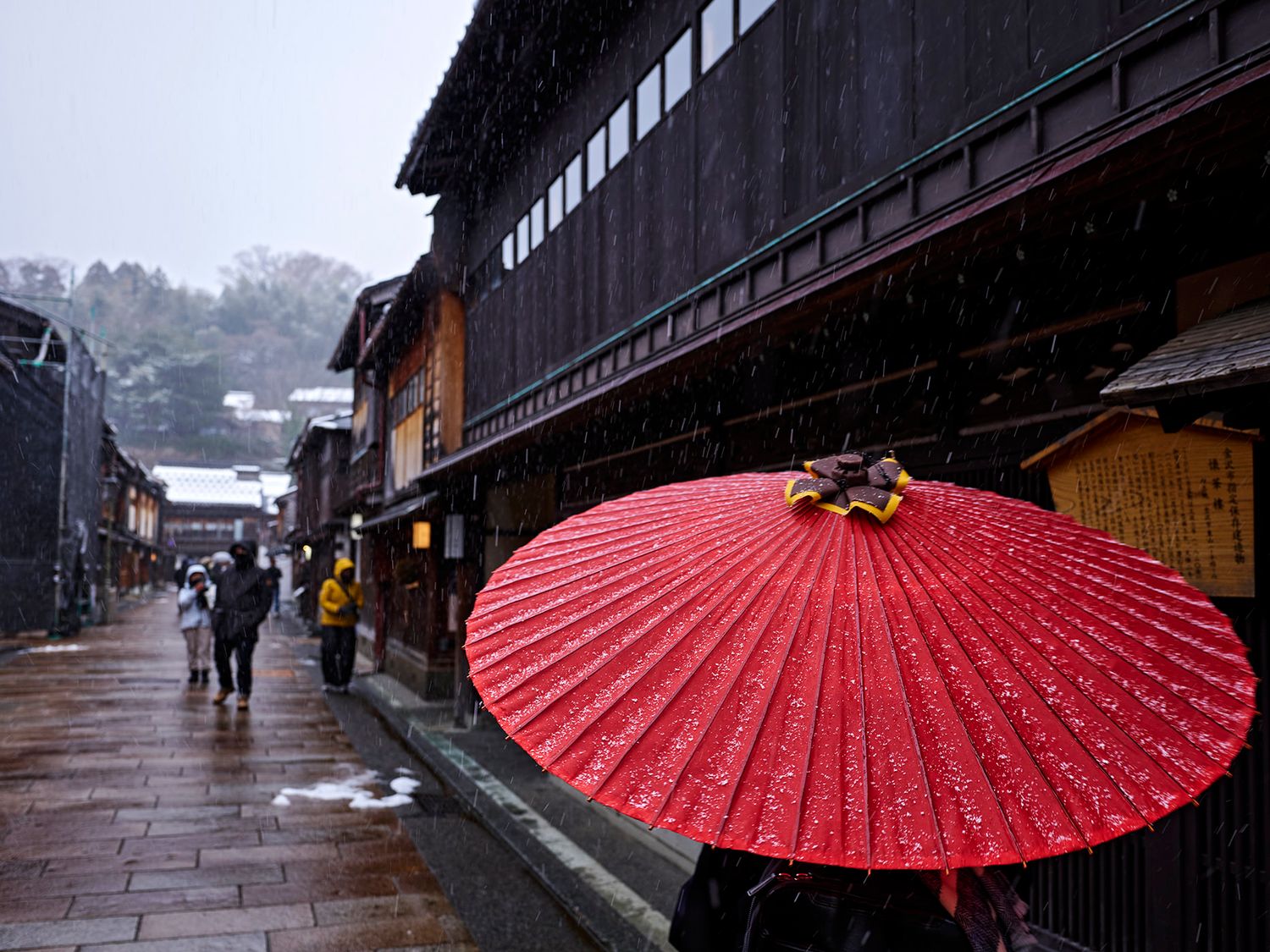 A vibrant red Japanese umbrella on a snowy street in a historic Japanese town with traditional wooden buildings.