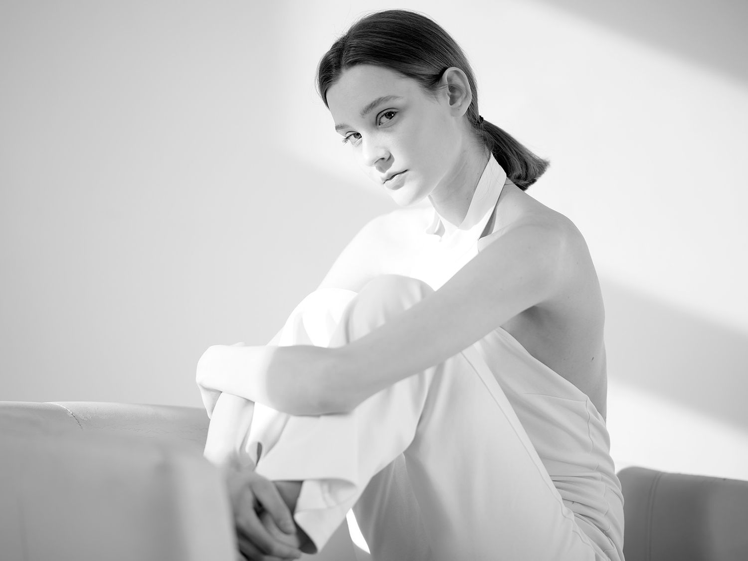 Black and white photo of a young woman in a white top sitting thoughtfully on a light-colored sofa.