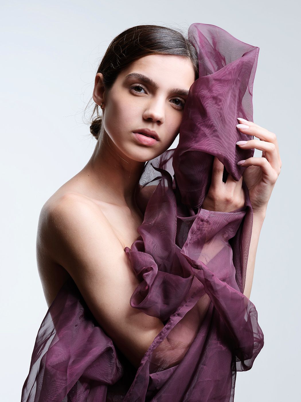 Young woman draped in flowing purple organza fabric, posing elegantly against a light gray background.