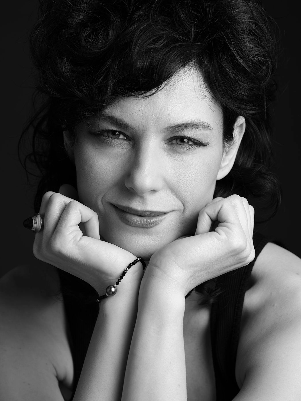 Black and white portrait of a curly-haired woman smiling with hands framing her face.