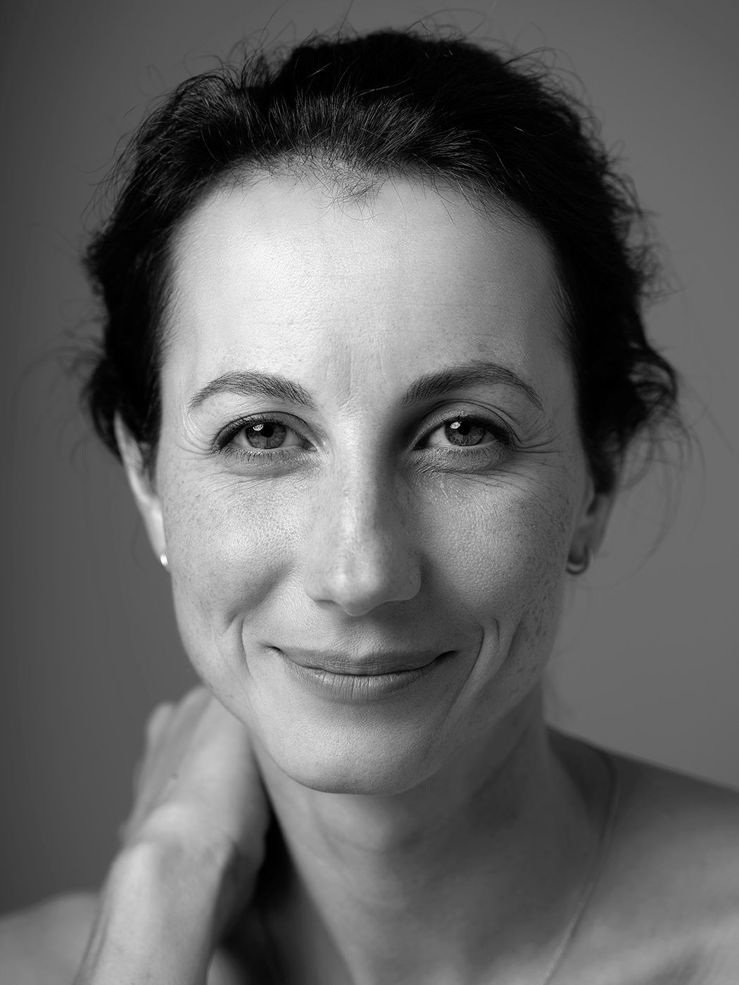 Black and white portrait of a smiling middle-aged woman with dark upswept hair touching her neck.