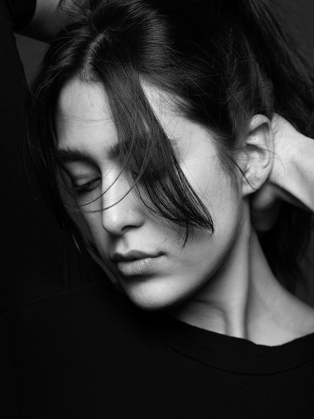 Black and white portrait of a young woman with dark hair, eyes closed, head tilted down in a contemplative pose.