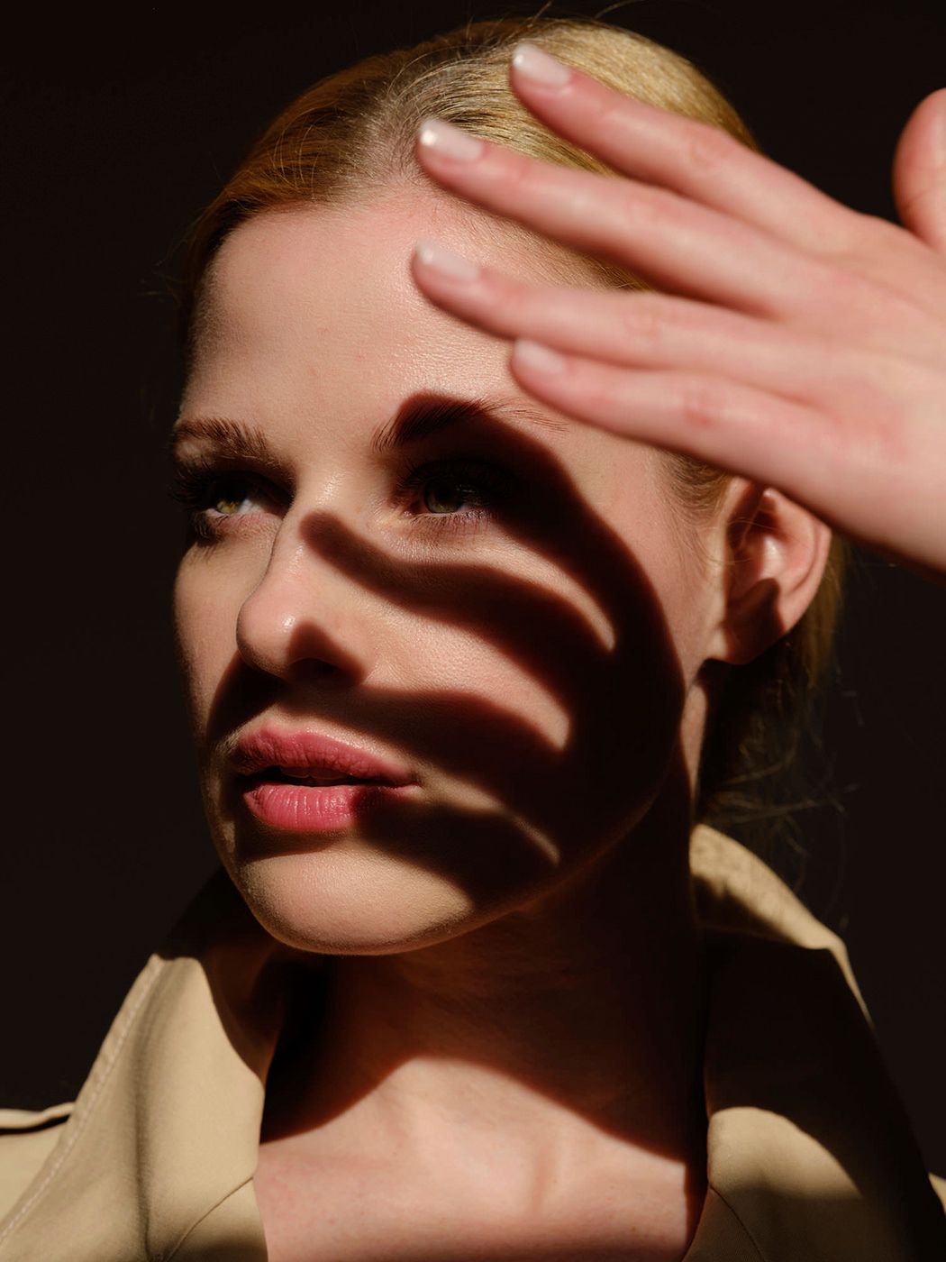 Woman shielding her face from sunlight with her hand, casting dramatic shadows across her features.