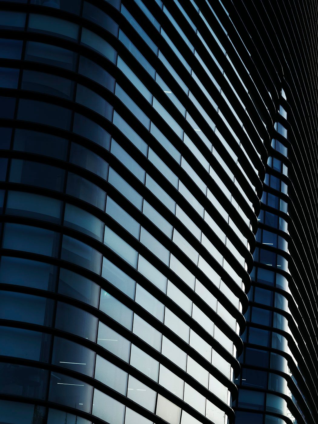 Close-up of a curved modern glass skyscraper facade with blue-tinted windows and dark steel frames.