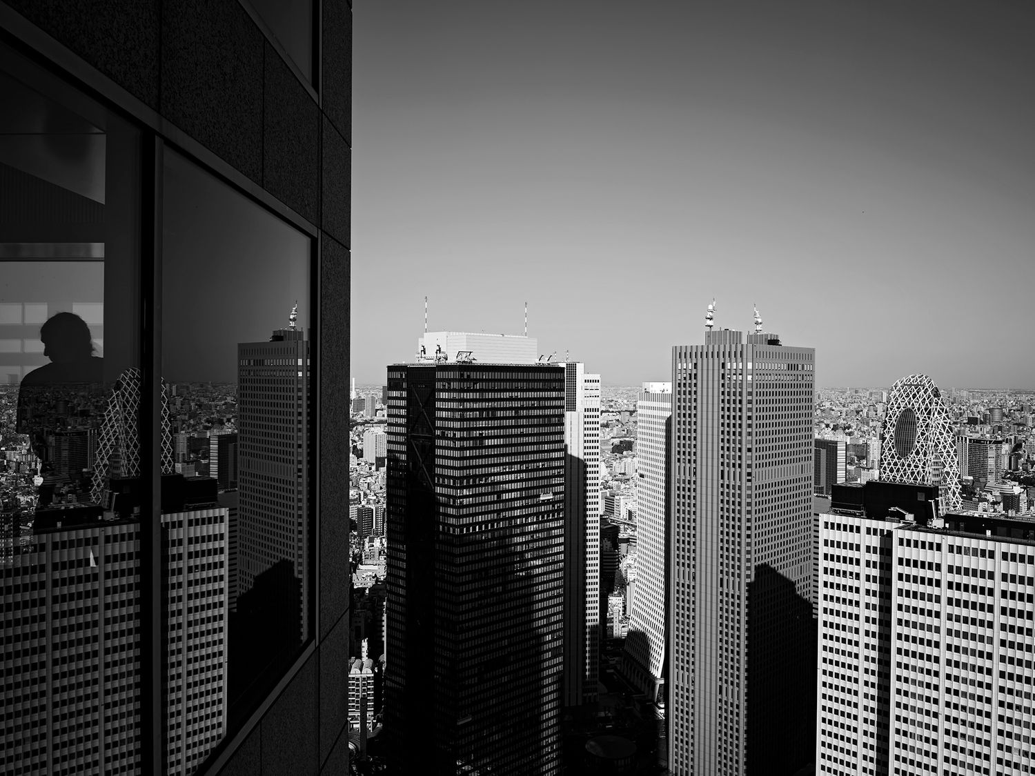 Black and white aerial cityscape with skyscrapers and a silhouette reflected in glass.
