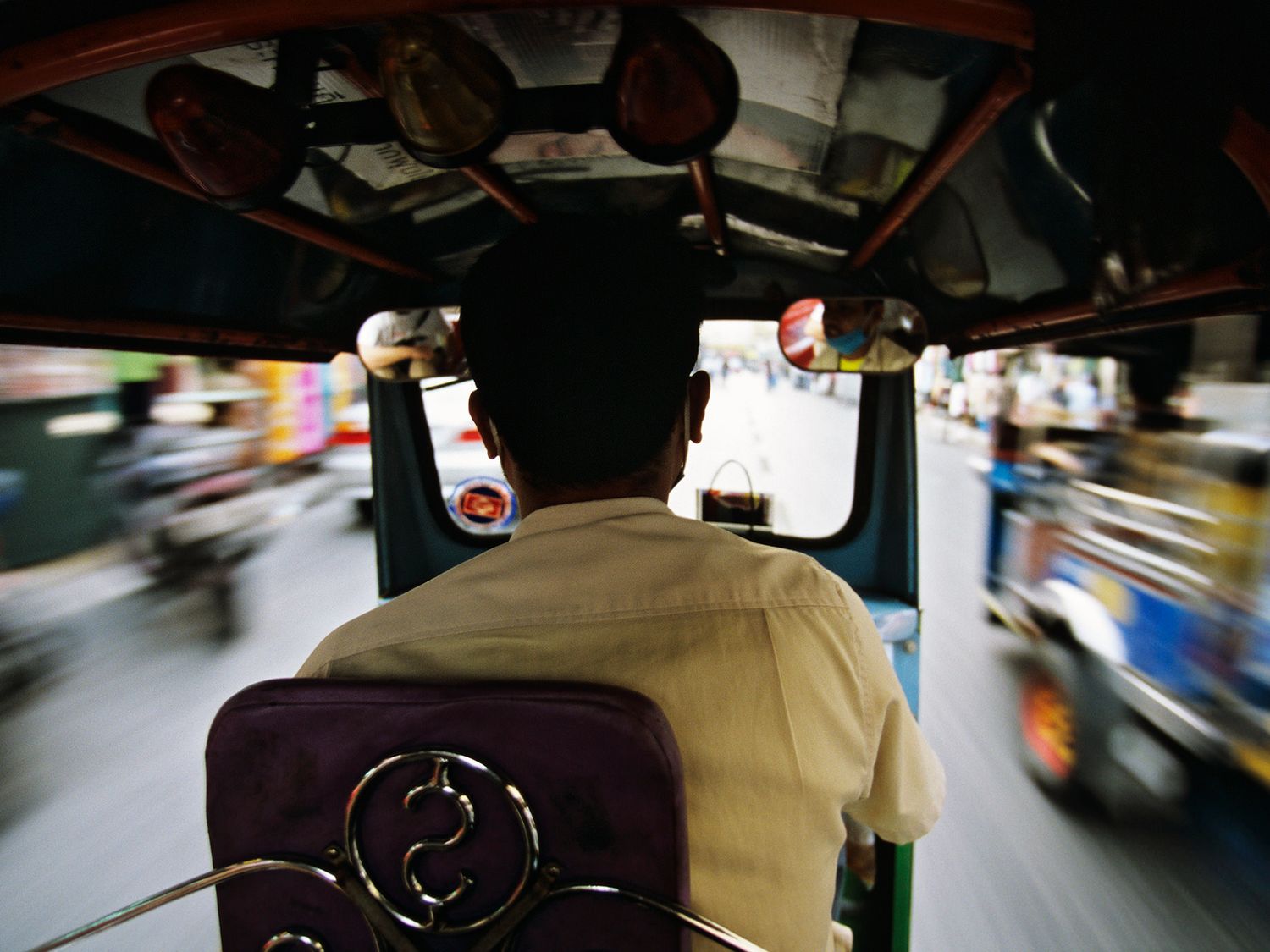 Rear view of a tuk-tuk driver navigating busy city traffic, captured with motion blur effect.