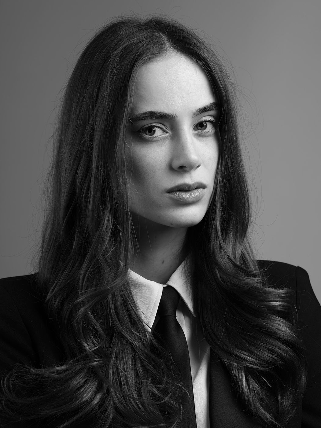Black and white portrait of a young woman with long wavy hair wearing a suit and tie, elegant professional look.