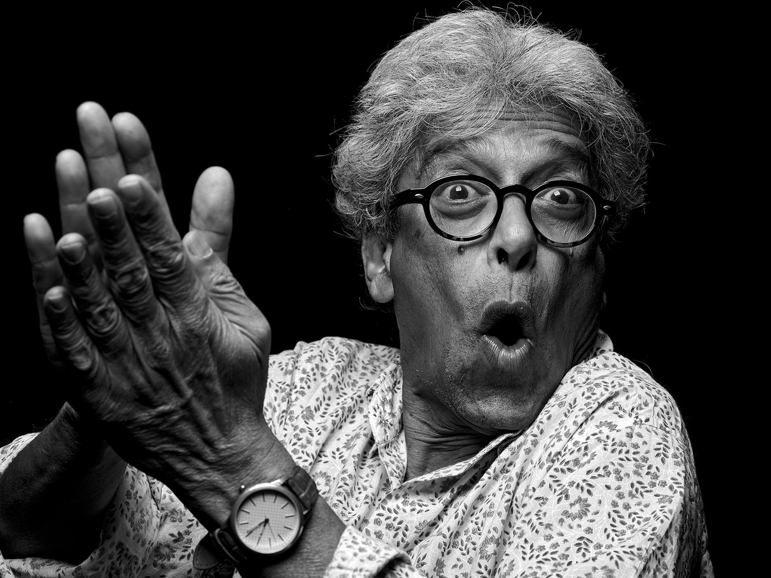 Black and white photo of an elderly man with glasses, looking surprised while clapping her hands. Trilok Gurtu, musician, percussionist.
