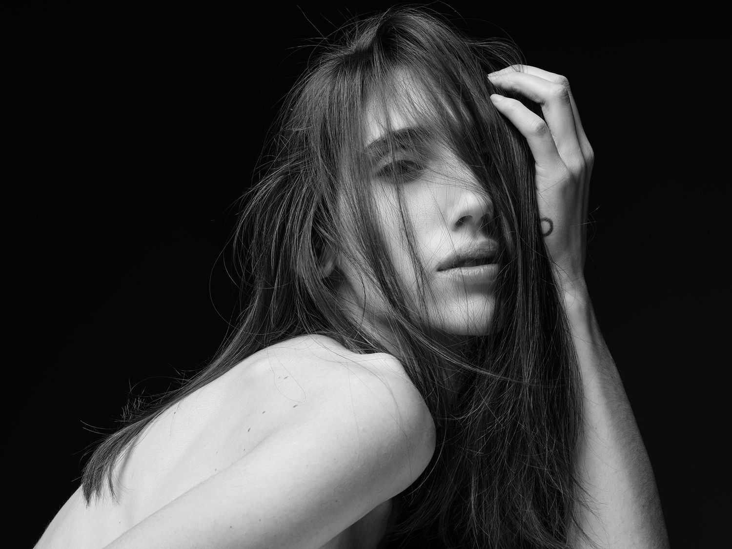 Black and white portrait of a woman with long hair posing dramatically against a dark background.