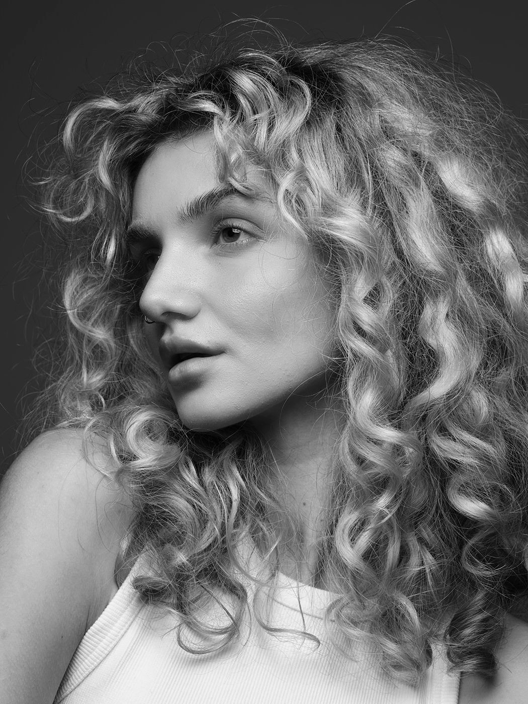 Black and white portrait of a young woman with long, voluminous curly blonde hair in a sleeveless top.