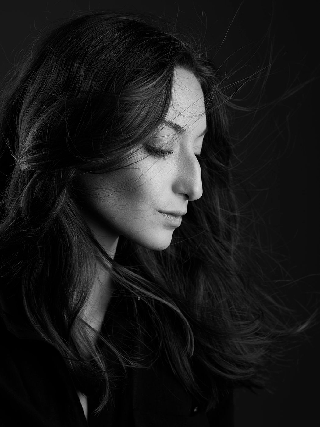 Black and white profile portrait of a woman with long flowing dark hair against a dark background.