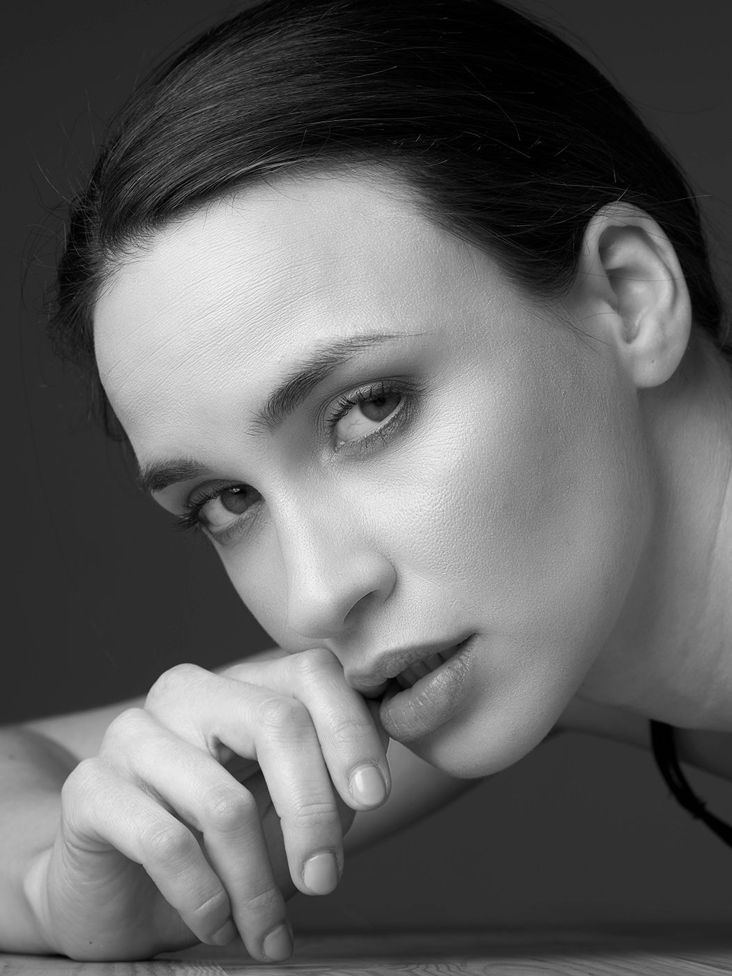 Black and white close-up portrait of a young woman resting her chin on her hand, gazing pensively at the camera.