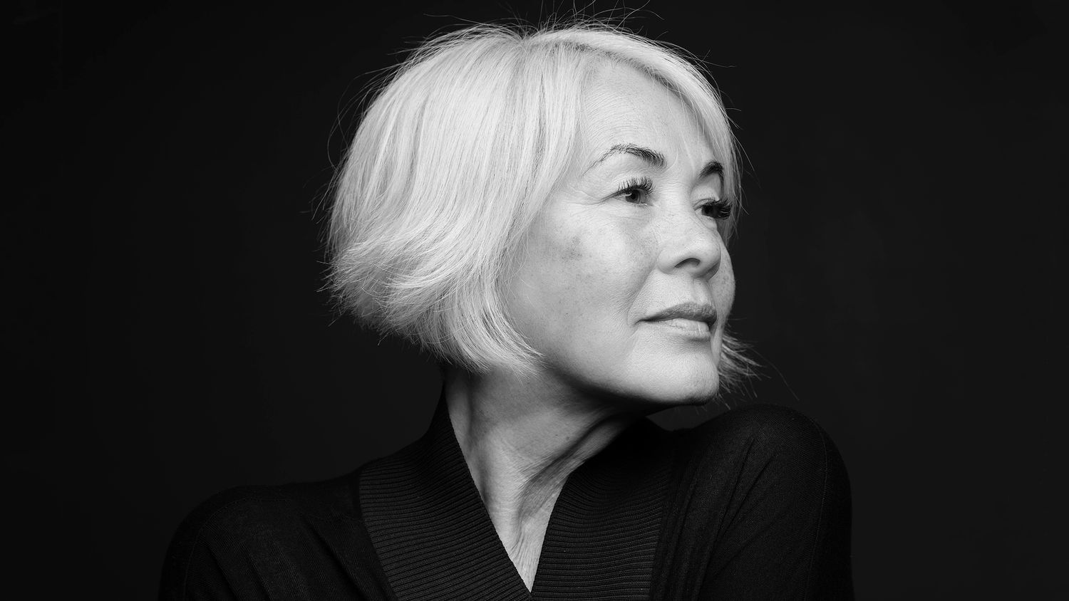 Elegant black and white portrait of an older woman with short white hair wearing a black top, looking sideways.