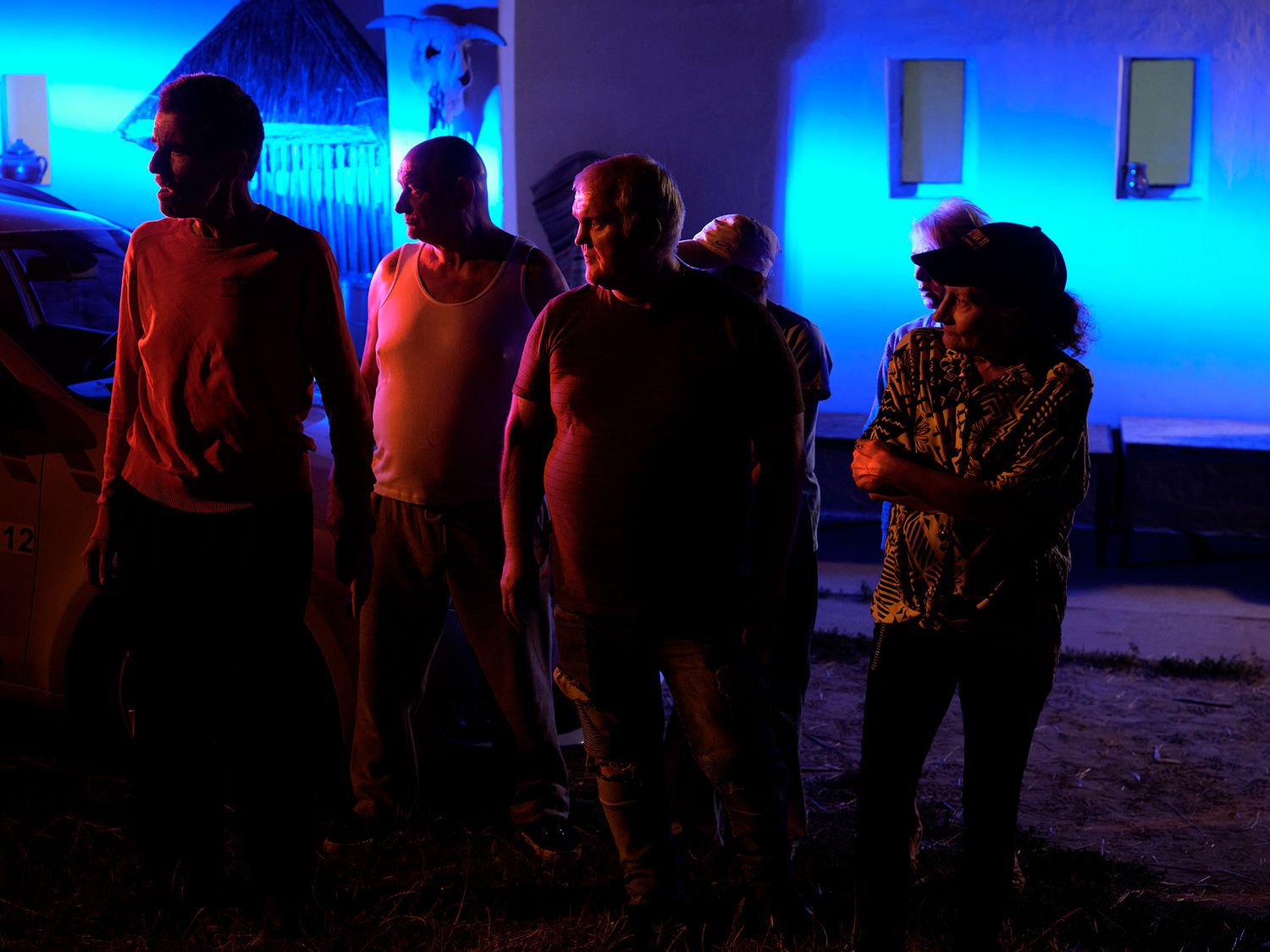 Group of people standing outdoors under dramatic blue and red lighting at night.
