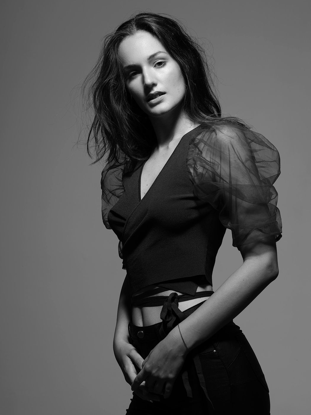 Black and white fashion portrait of a woman in a sheer puff-sleeve top and dark jeans posing confidently.