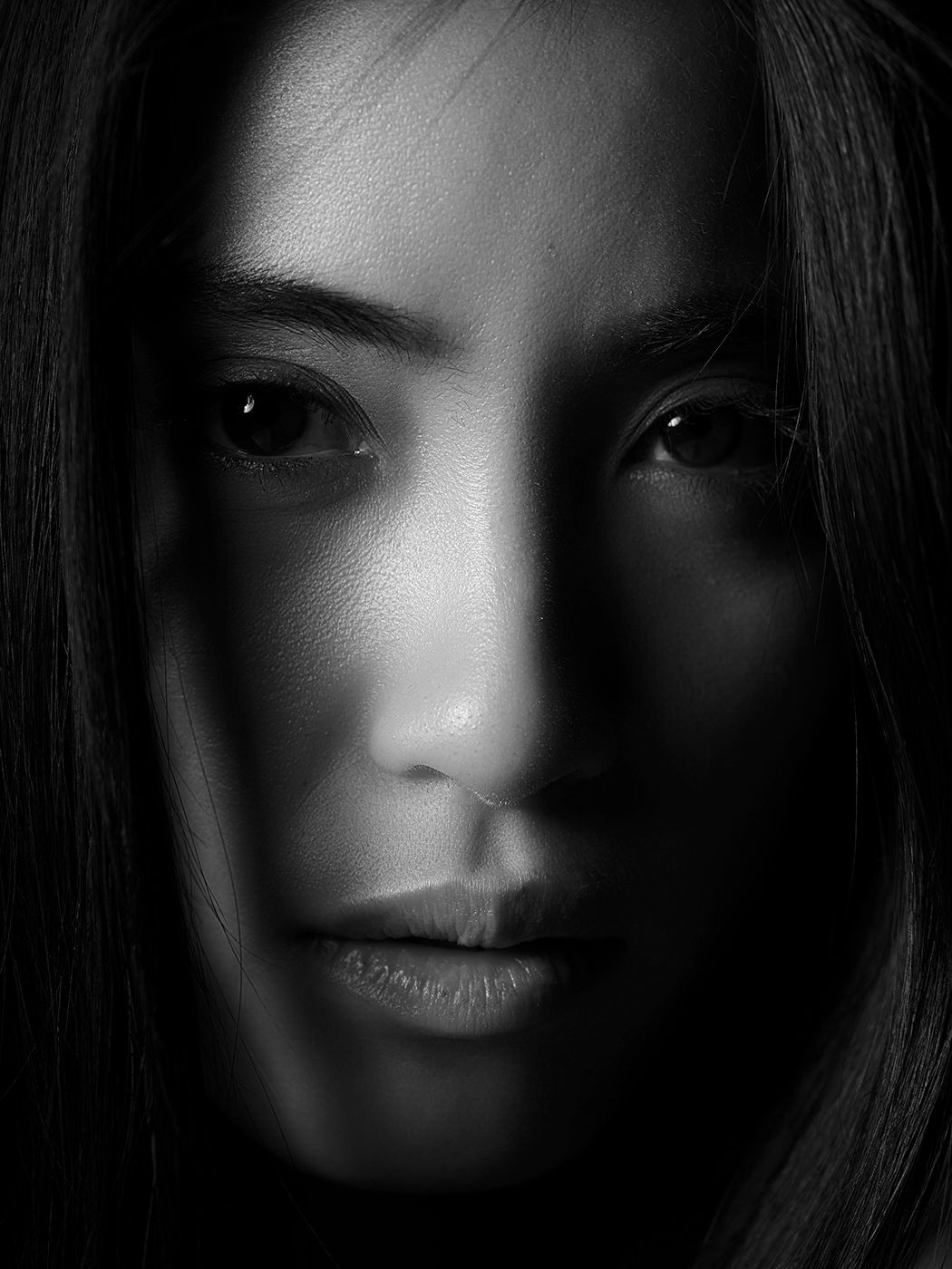 Black and white close-up portrait of a woman with dark hair, dramatic shadow lighting across her face.