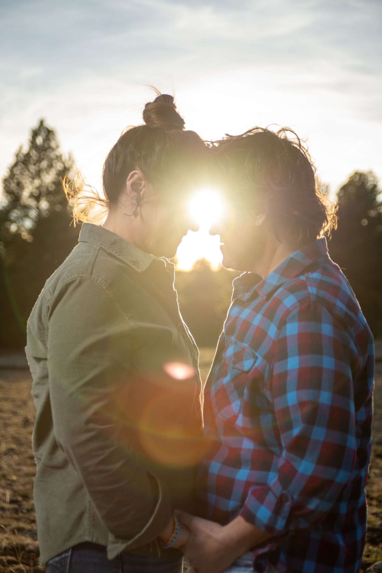 Couple embracing forehead to forehead at golden hour with sun flare between them outdoors.