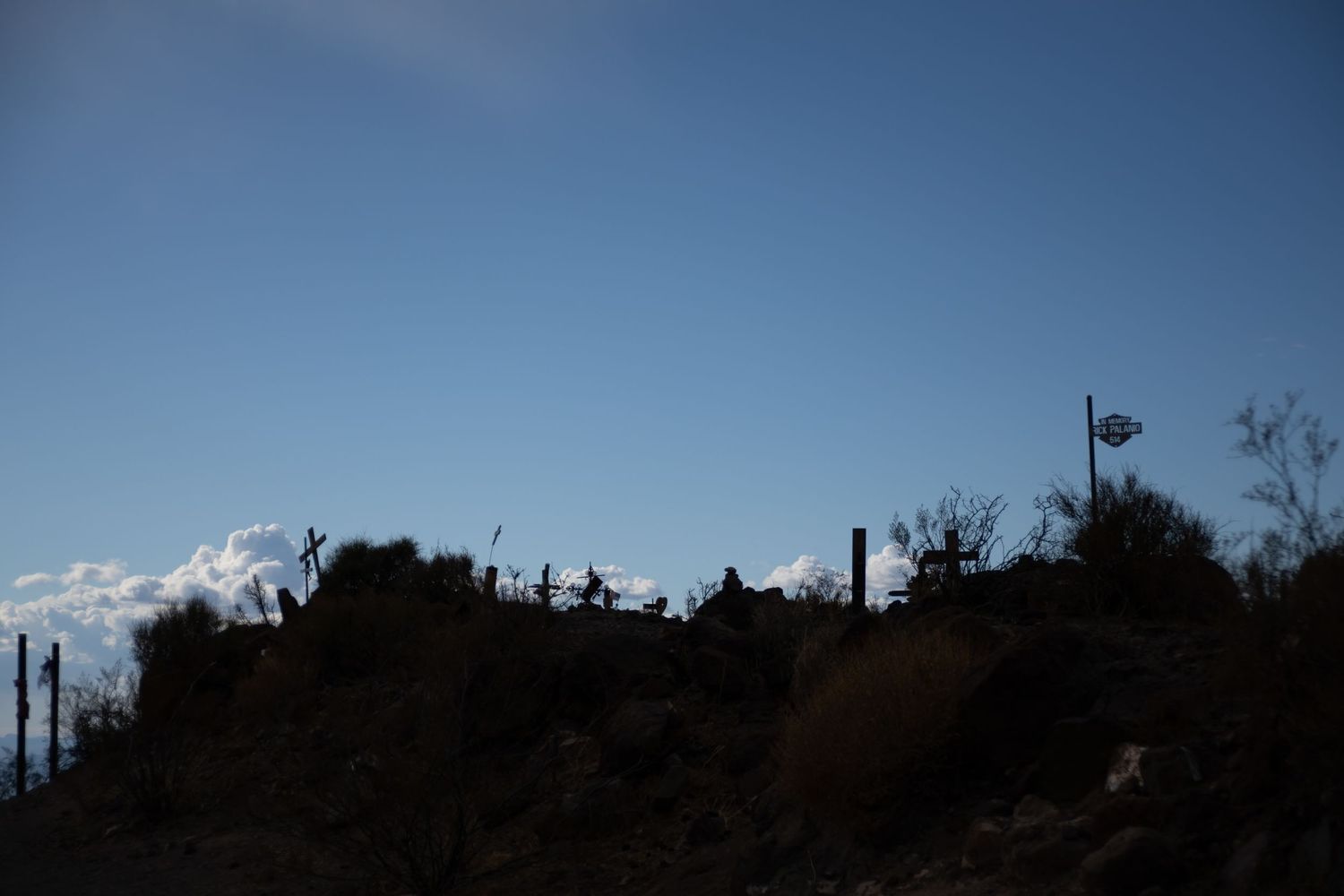 Silhouetted desert landscape at dusk with crosses and a flag against a blue sky.