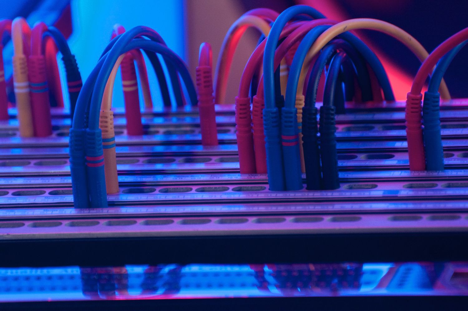 Colorful network cables plugged into server rack equipment illuminated by blue and pink lighting.