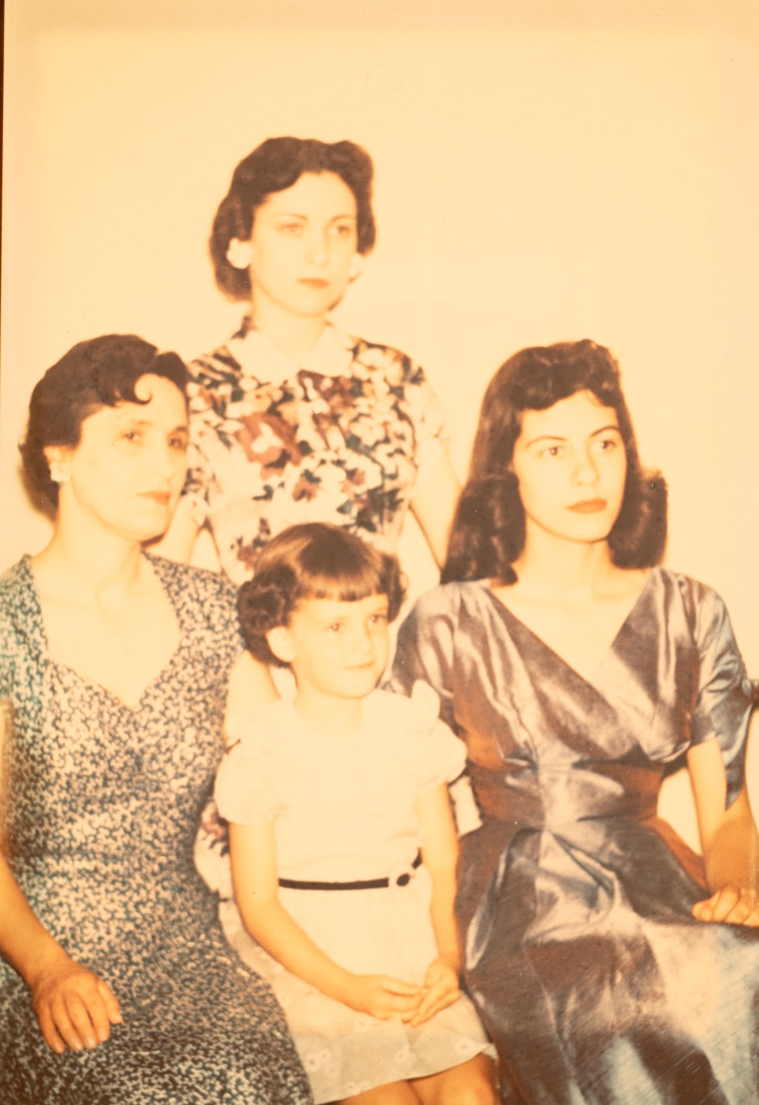 Antique colorized family photo featuring three women and a young child posing for a portrait.
