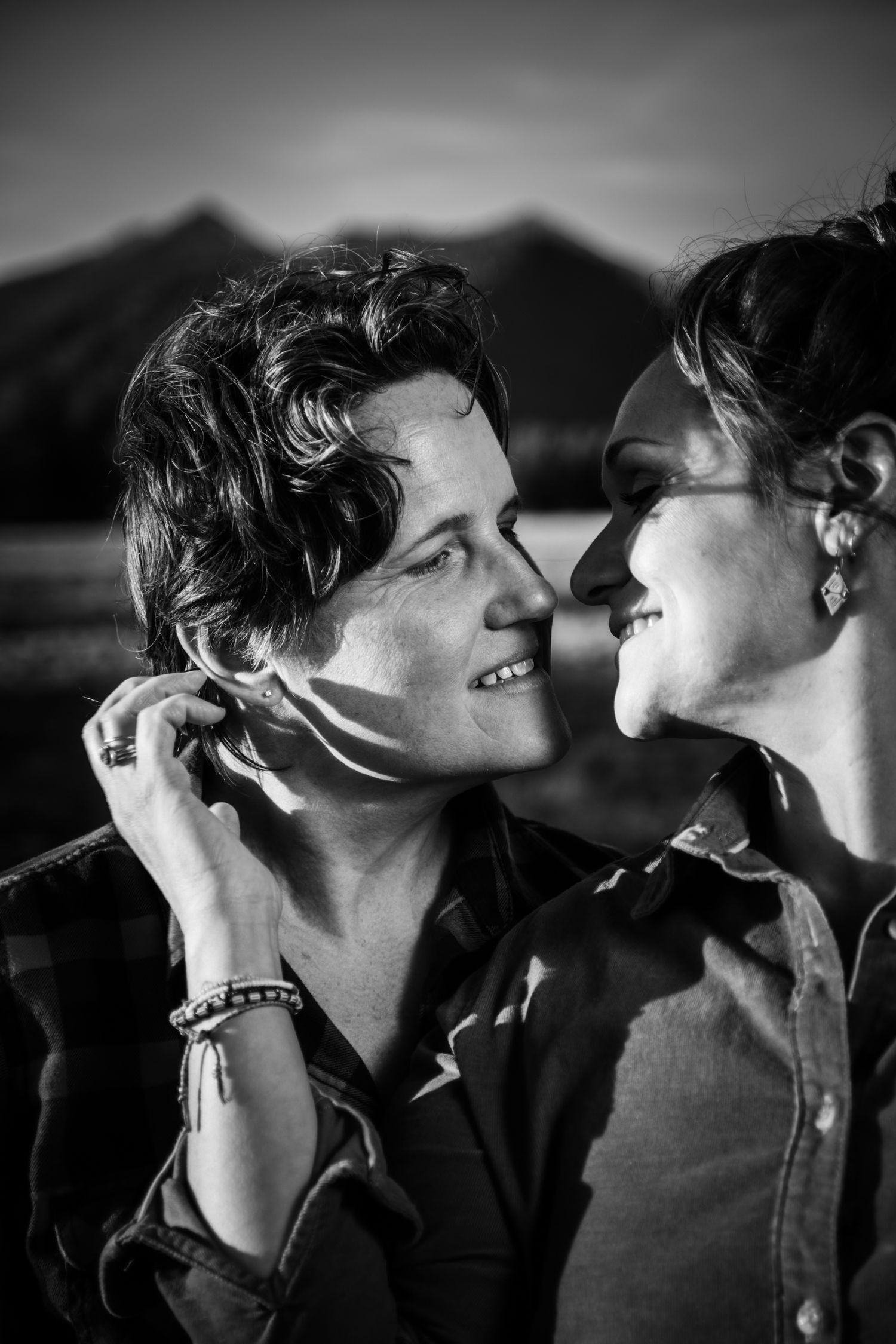 Black and white portrait of two women smiling and facing each other in warm outdoor lighting.