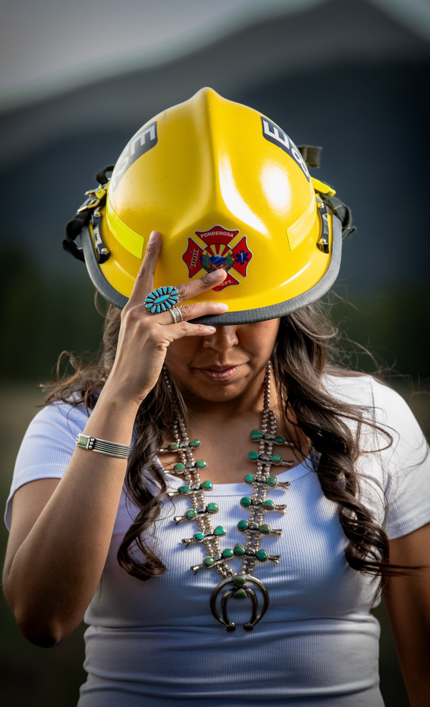 Native American woman wearing yellow firefighter helmet and traditional turquoise squash blossom necklace.