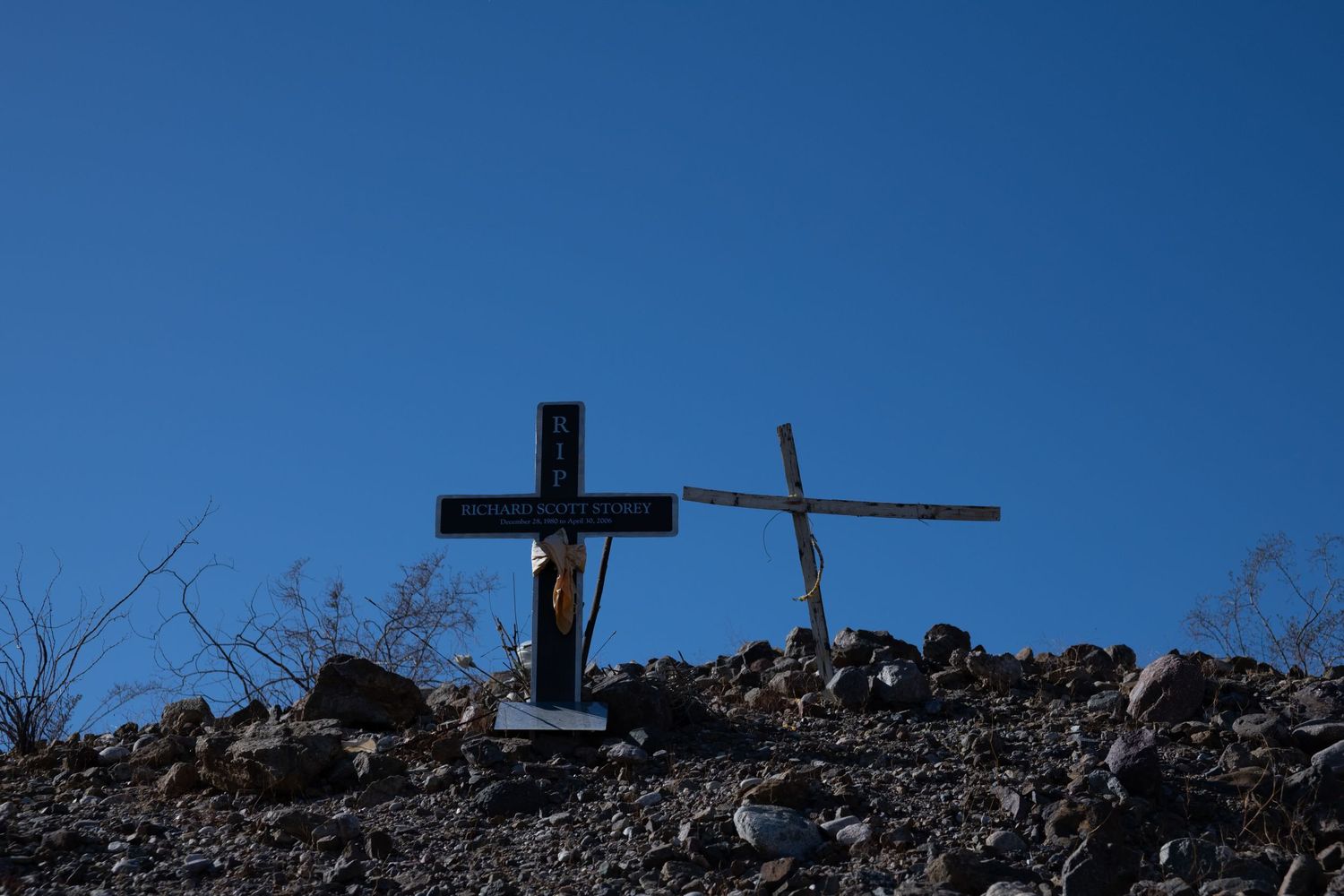 Two memorial crosses silhouetted against bright blue sky on rocky desert hillside.