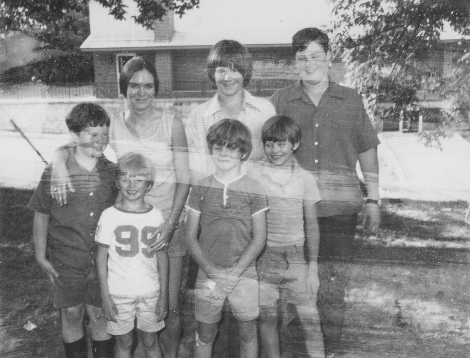 Black and white family photo of seven children posing together outdoors in front of a suburban house.