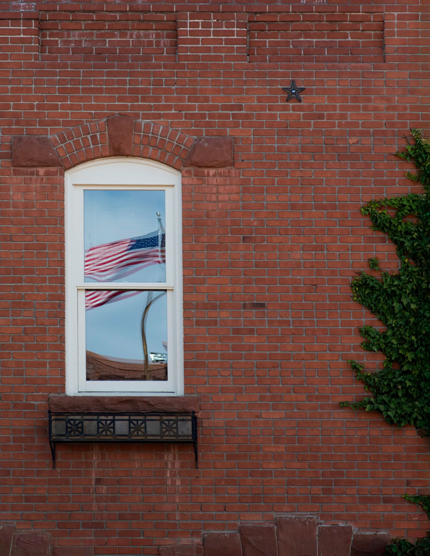 American flag reflected in an arched window of a classic red brick building with ivy.