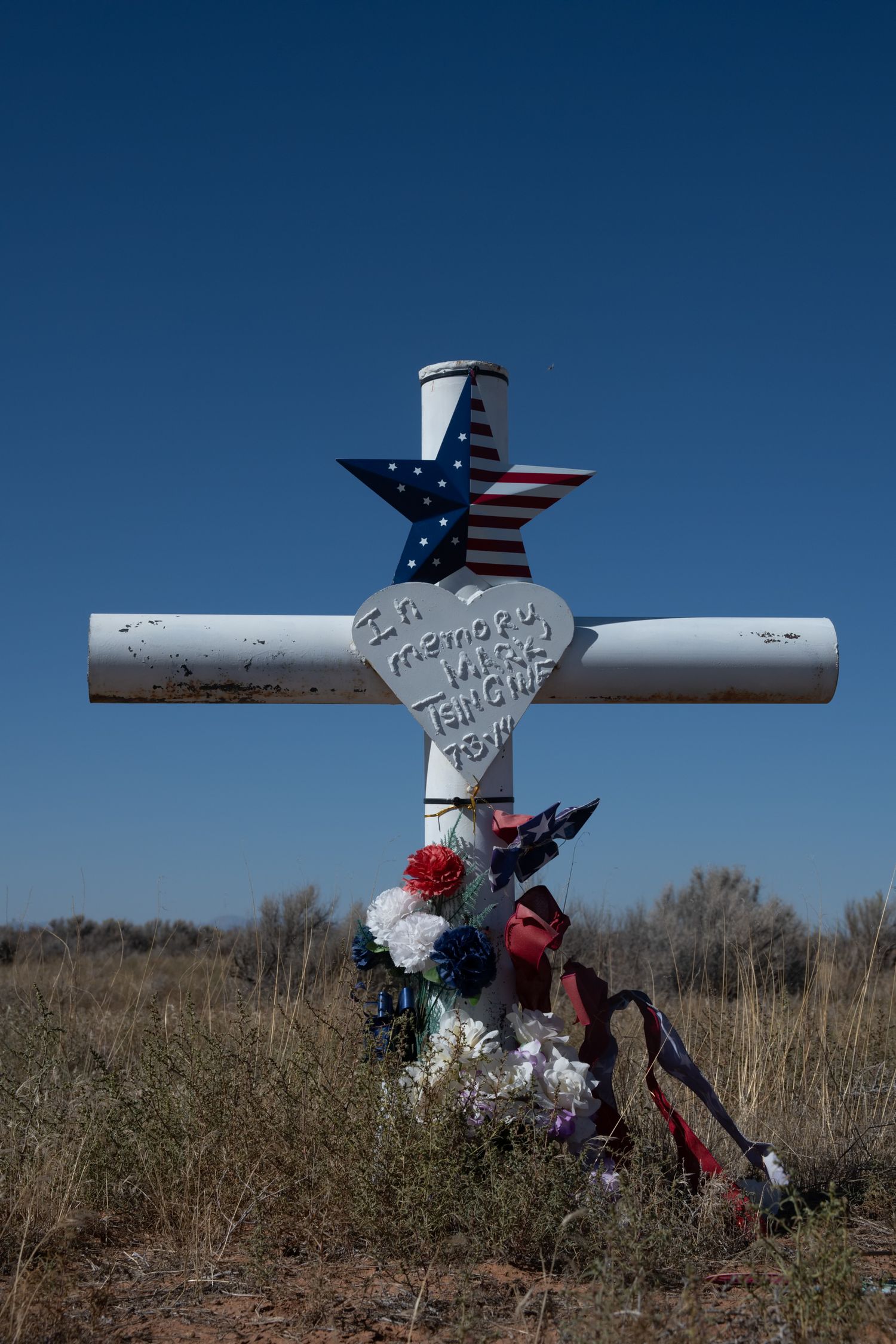 White roadside memorial cross with American flag star reading In Memory in an open field.