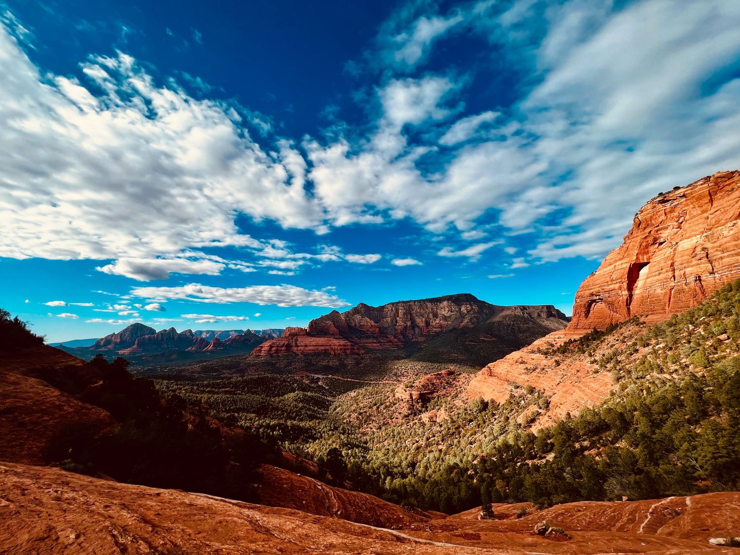 Red rock canyon landscape in Sedona Arizona with dramatic blue sky and white clouds over rust colored buttes.
