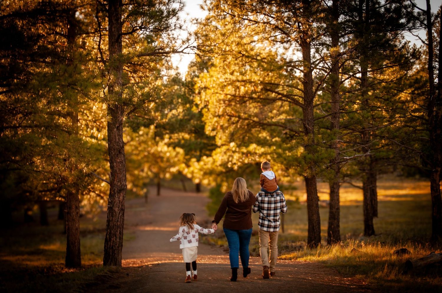 Family walking hand-in-hand down a tree-lined path surrounded by vibrant autumn foliage at sunset.
