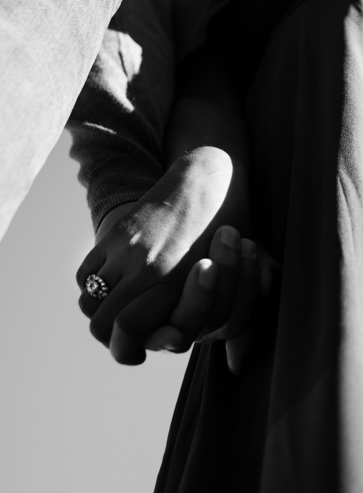 Black and white close-up of two hands holding with decorative ring in soft light.
