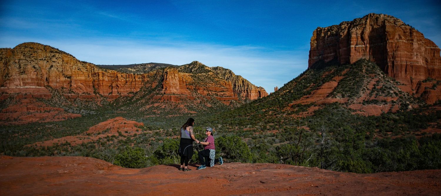 Two people with a stroller overlook stunning red rock formations and green valley in Sedona, Arizona.