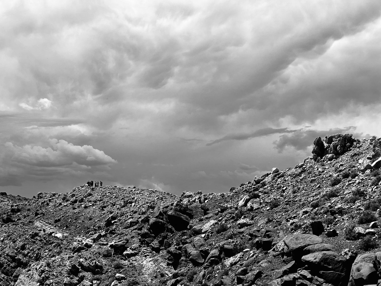 Dramatic storm clouds loom over a rocky mountainous landscape in a striking black and white landscape photograph.