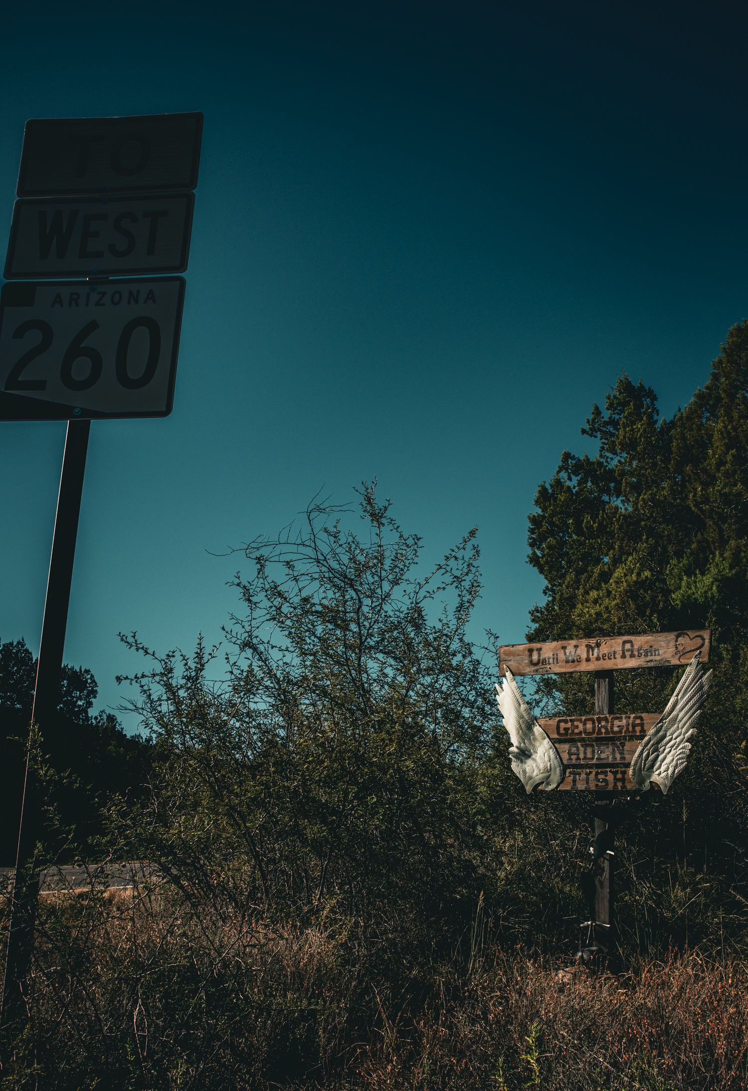 Roadside memorial with angel wings near Arizona State Route 260 West highway sign at dusk.
