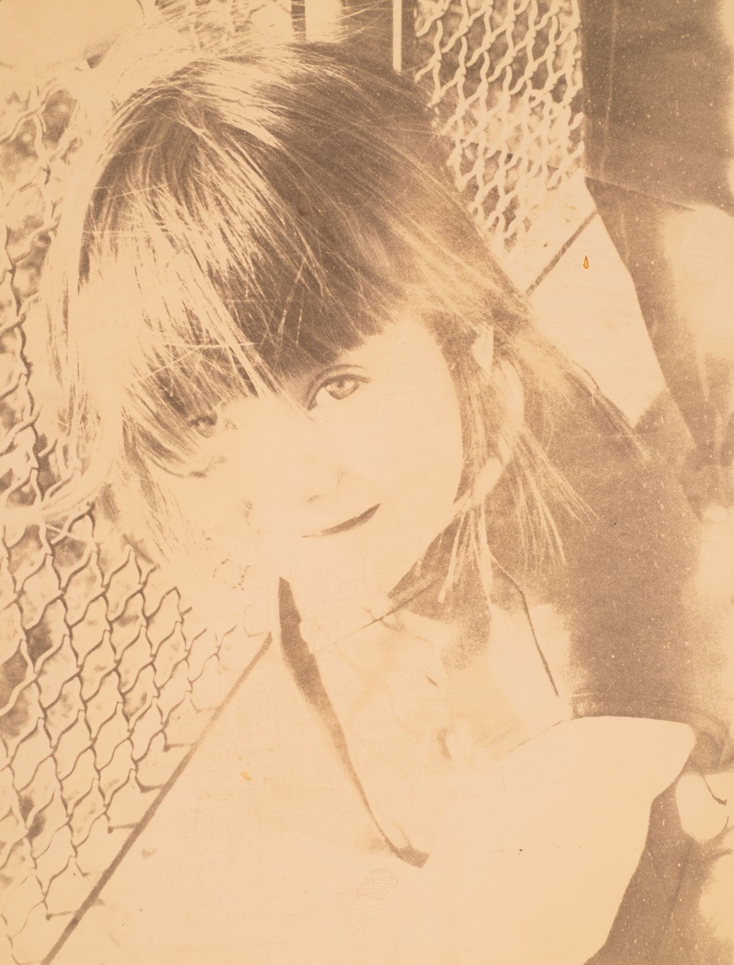 Vintage sepia-toned portrait of a young woman with bangs posing near a chain-link fence.